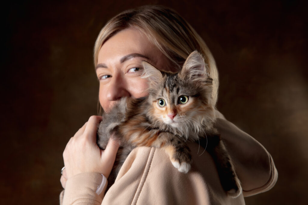 A young woman smiling with a small kitten sitting on her shoulder.